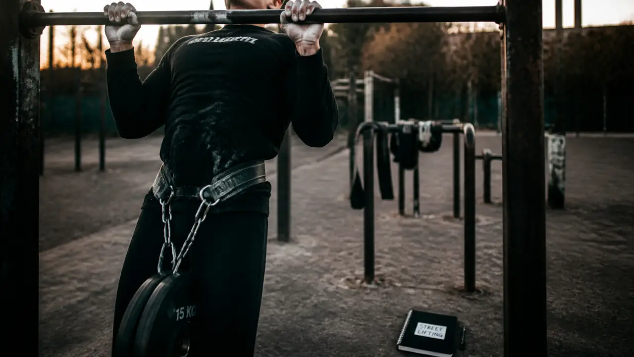 Street lifting : athlète en traction lestée sur barre fixe, dip belt et chalk